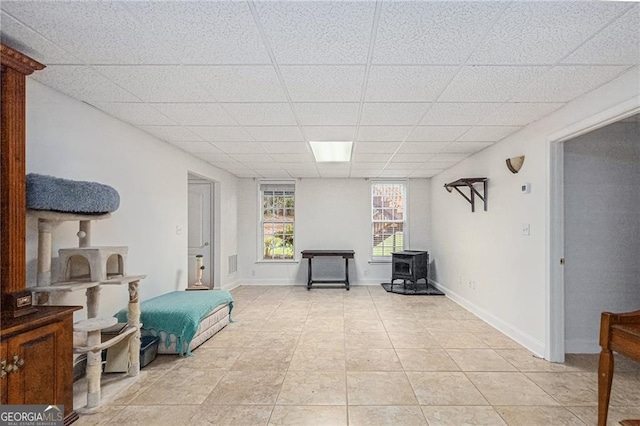 sitting room with light tile patterned floors, a wood stove, and a drop ceiling