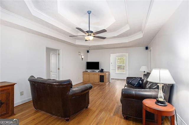 living room featuring light wood-type flooring, a raised ceiling, ceiling fan, and crown molding