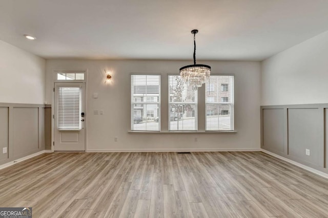 unfurnished dining area featuring a chandelier and light hardwood / wood-style floors