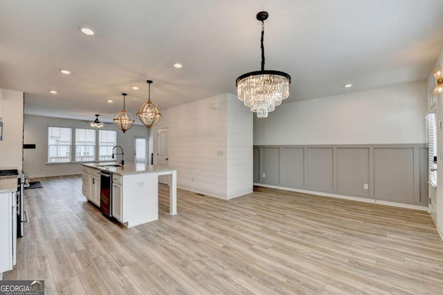 kitchen with white cabinetry, light stone countertops, an island with sink, decorative light fixtures, and light wood-type flooring