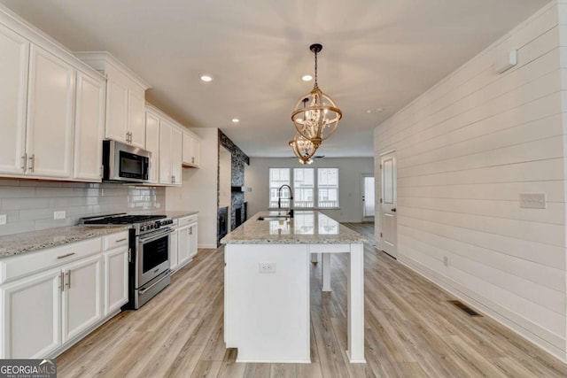 kitchen with stainless steel appliances, a kitchen island with sink, sink, white cabinets, and light hardwood / wood-style floors