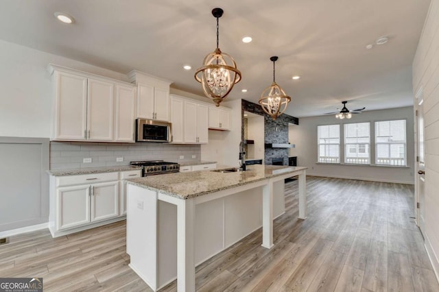 kitchen with white cabinets, ceiling fan with notable chandelier, a center island with sink, and stainless steel appliances