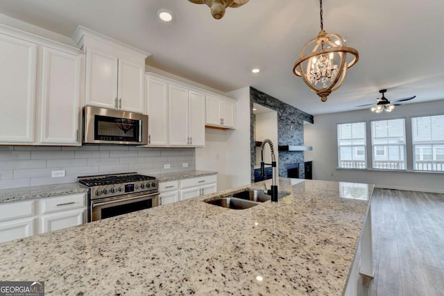 kitchen with sink, stainless steel appliances, light hardwood / wood-style floors, white cabinets, and ceiling fan with notable chandelier