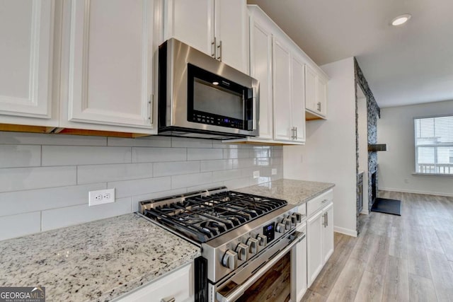 kitchen featuring light stone countertops, light wood-type flooring, stainless steel appliances, and white cabinetry