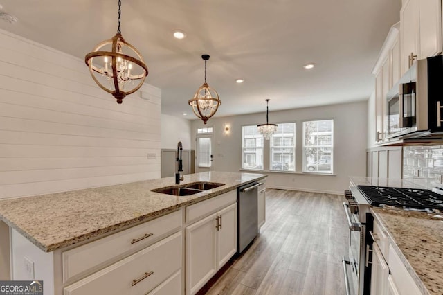 kitchen with appliances with stainless steel finishes, sink, a notable chandelier, light hardwood / wood-style floors, and white cabinetry