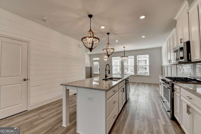 kitchen featuring white cabinetry, sink, hanging light fixtures, stainless steel appliances, and a center island with sink