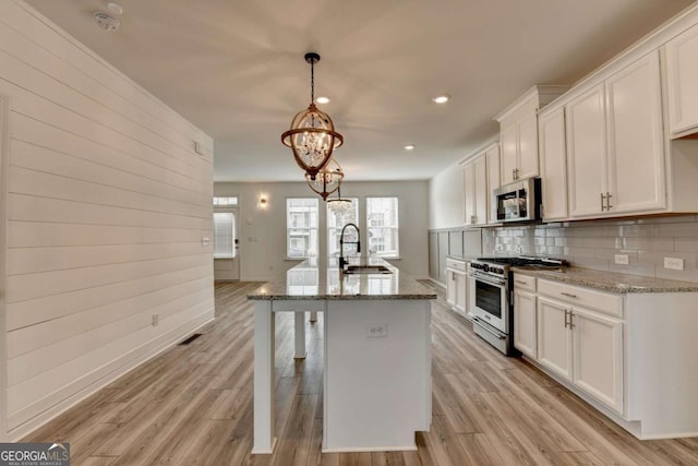 kitchen with white cabinets, light stone countertops, appliances with stainless steel finishes, and light hardwood / wood-style flooring