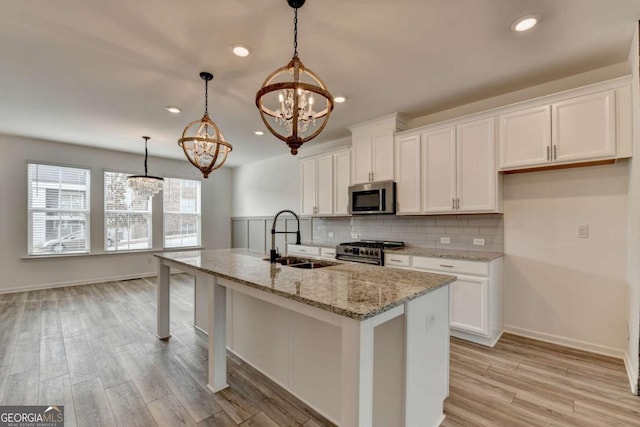 kitchen with white cabinetry, an island with sink, stainless steel appliances, and decorative light fixtures