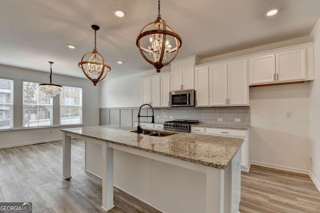 kitchen with pendant lighting, a kitchen island with sink, a notable chandelier, white cabinetry, and stainless steel appliances