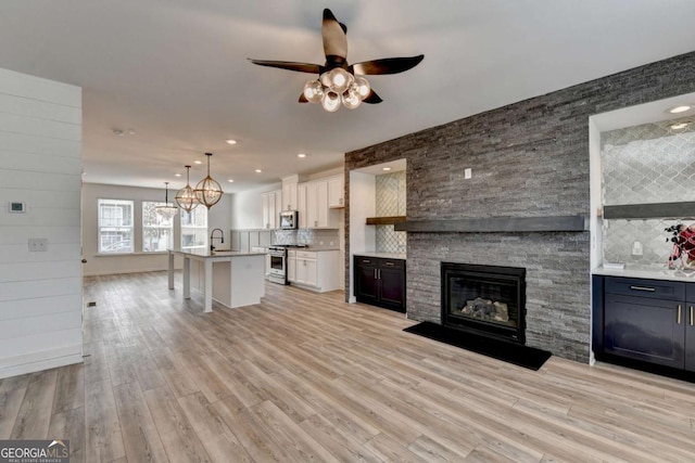 unfurnished living room featuring ceiling fan with notable chandelier, sink, a fireplace, and light hardwood / wood-style flooring