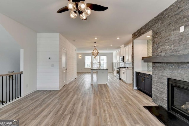 unfurnished living room featuring ceiling fan, sink, light wood-type flooring, and a fireplace