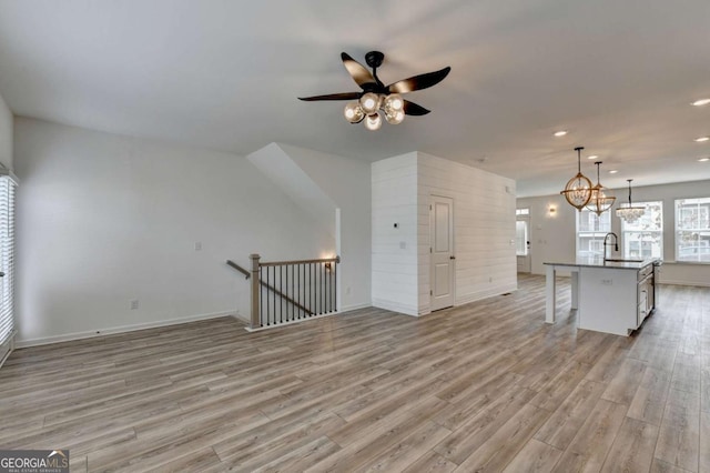 unfurnished living room with ceiling fan with notable chandelier, light wood-type flooring, and sink