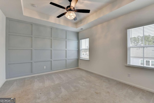 carpeted empty room featuring a tray ceiling, plenty of natural light, and ceiling fan