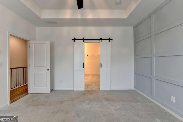 unfurnished bedroom with a raised ceiling, a barn door, and light colored carpet