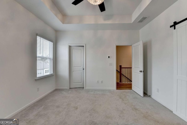 unfurnished bedroom with a raised ceiling, ceiling fan, a barn door, and light colored carpet