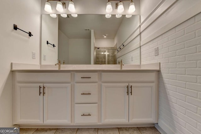 bathroom with tile patterned flooring, vanity, a shower with shower door, and brick wall