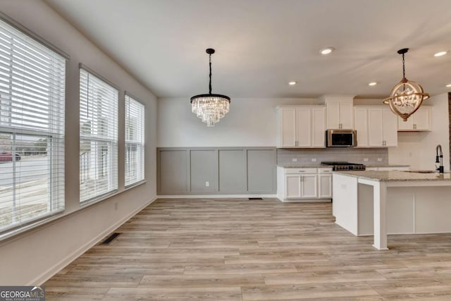 kitchen featuring pendant lighting, white cabinets, light stone countertops, stainless steel appliances, and a chandelier