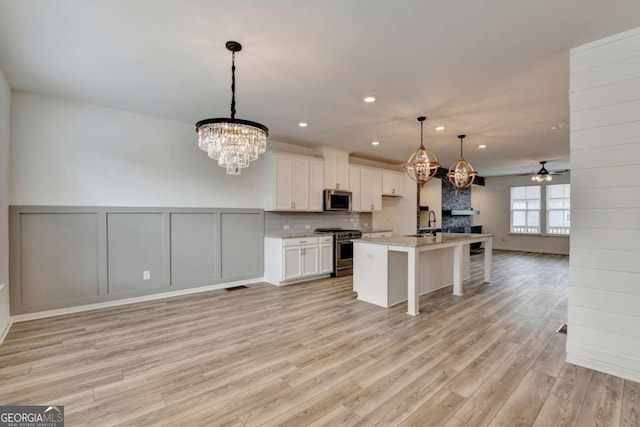 kitchen with stainless steel appliances, decorative light fixtures, white cabinets, light hardwood / wood-style floors, and an island with sink