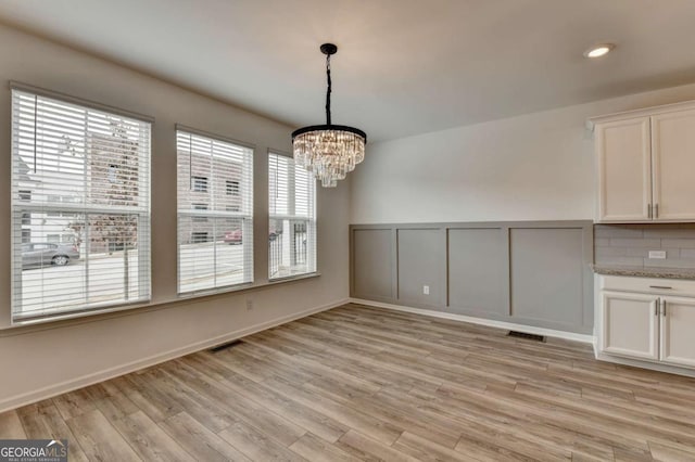 unfurnished dining area featuring a notable chandelier and light hardwood / wood-style floors