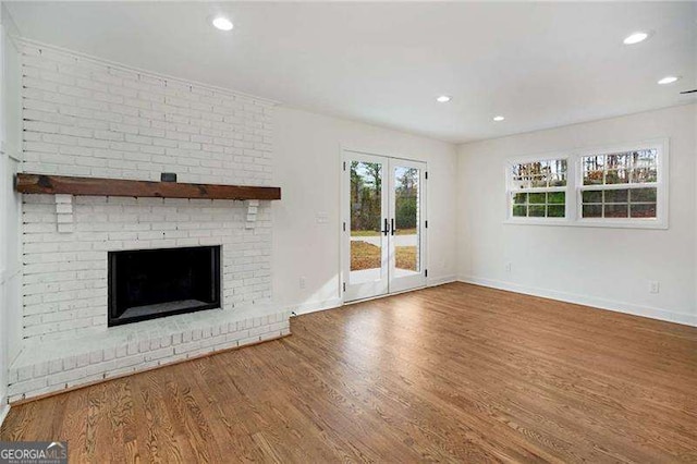 unfurnished living room featuring french doors, wood-type flooring, and a brick fireplace