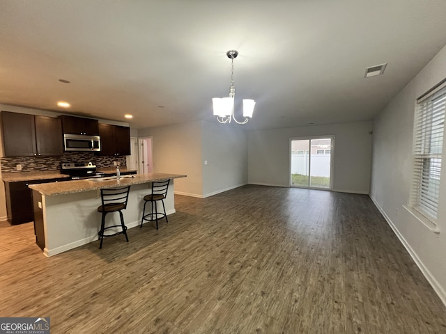 kitchen featuring a kitchen bar, stainless steel appliances, a kitchen island with sink, decorative light fixtures, and hardwood / wood-style floors