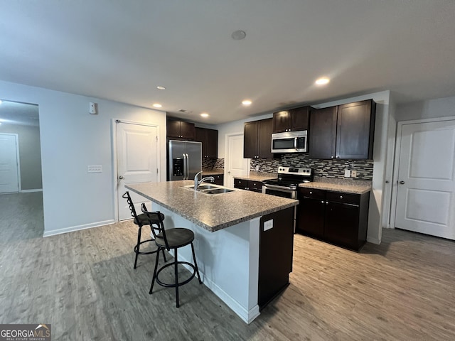 kitchen with sink, light hardwood / wood-style flooring, a kitchen bar, a kitchen island with sink, and appliances with stainless steel finishes