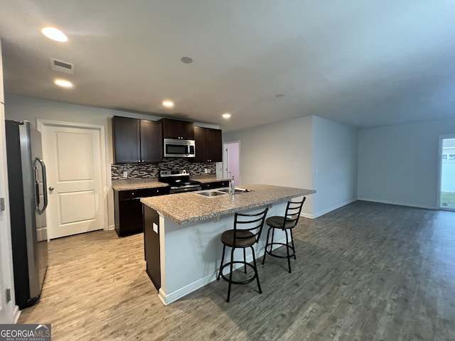 kitchen featuring appliances with stainless steel finishes, a breakfast bar, sink, light hardwood / wood-style flooring, and an island with sink