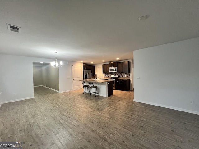 interior space with a kitchen island with sink, appliances with stainless steel finishes, tasteful backsplash, dark hardwood / wood-style flooring, and a breakfast bar area