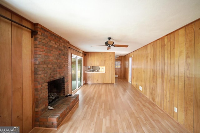 unfurnished living room with a brick fireplace, light hardwood / wood-style flooring, ceiling fan, and wooden walls