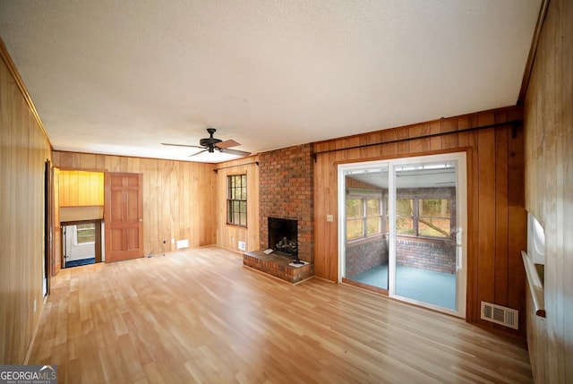 unfurnished living room featuring ceiling fan, light wood-type flooring, wooden walls, and a brick fireplace