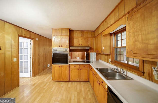 kitchen with wood walls, black electric stovetop, oven, sink, and light wood-type flooring