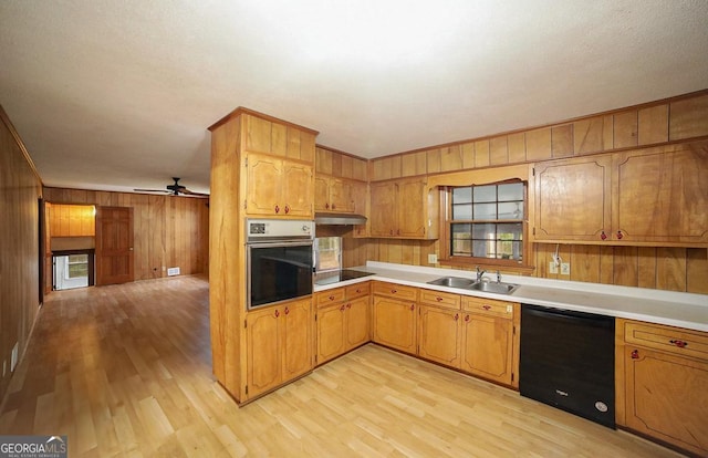 kitchen with black appliances, light hardwood / wood-style floors, sink, and wooden walls