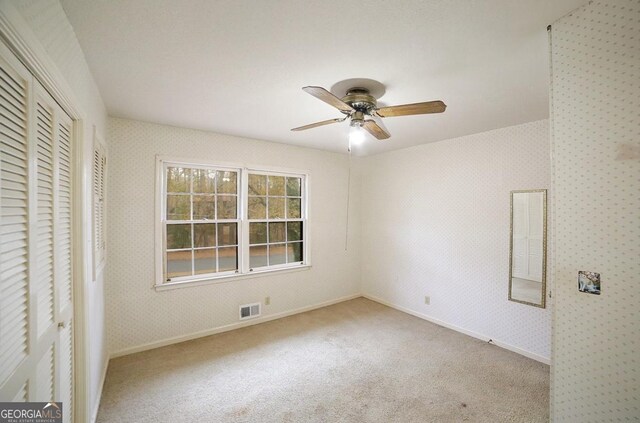 unfurnished bedroom featuring a closet, light colored carpet, and ceiling fan