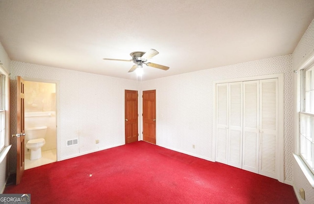 unfurnished bedroom featuring multiple windows, ceiling fan, carpet, and ensuite bathroom