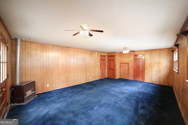 empty room featuring wooden walls, ceiling fan, and dark colored carpet