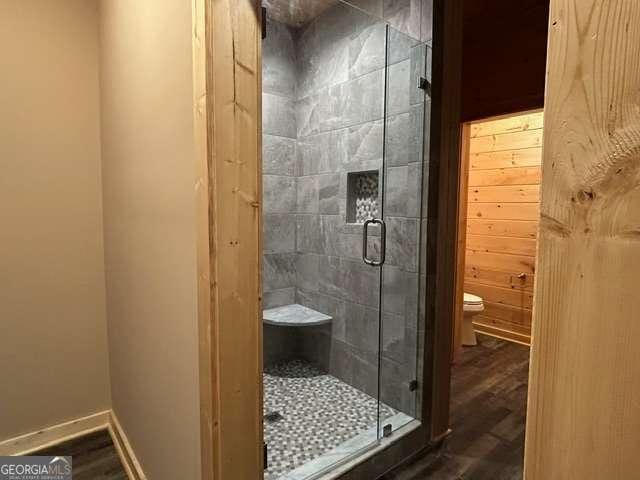 bathroom with hardwood / wood-style floors, wood walls, toilet, and a shower with door