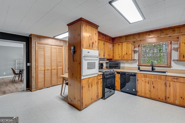 kitchen with black appliances, wood walls, ornamental molding, and sink