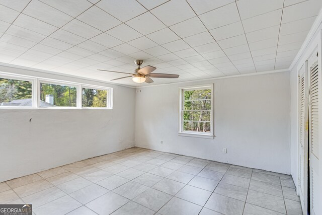 tiled empty room featuring ceiling fan and ornamental molding