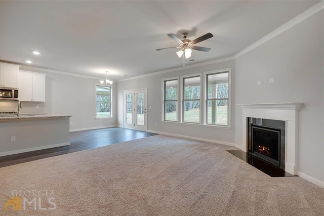 unfurnished living room featuring dark carpet, french doors, ceiling fan with notable chandelier, ornamental molding, and sink