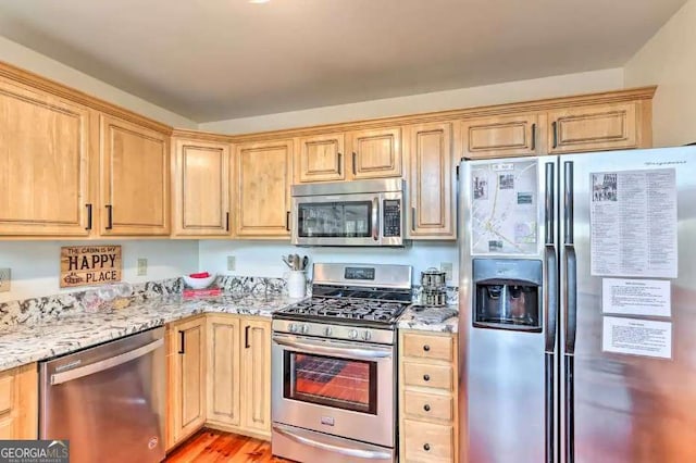 kitchen with light stone counters, light brown cabinets, stainless steel appliances, and light wood-type flooring