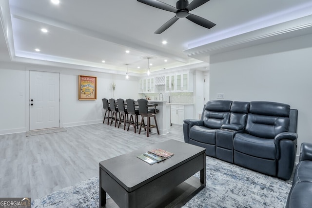 living room with light wood-type flooring, a tray ceiling, ceiling fan, and sink