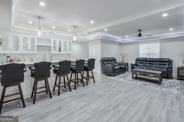 interior space featuring ceiling fan, a raised ceiling, light hardwood / wood-style flooring, and bar area