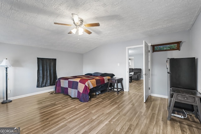 bedroom featuring ceiling fan, light hardwood / wood-style floors, a textured ceiling, and stainless steel refrigerator