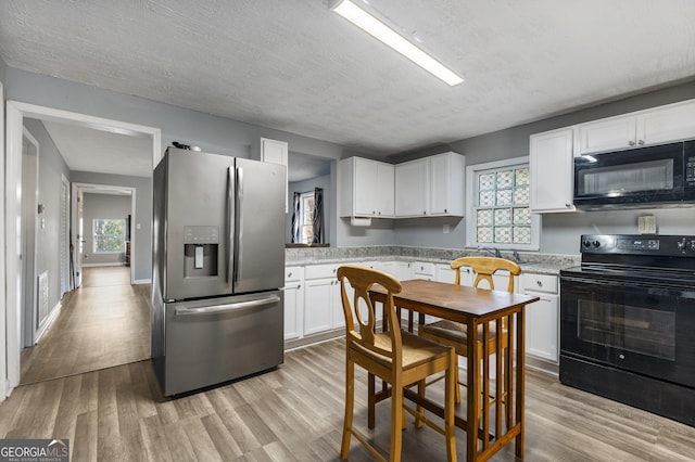 kitchen featuring a textured ceiling, light wood-type flooring, white cabinetry, and black appliances