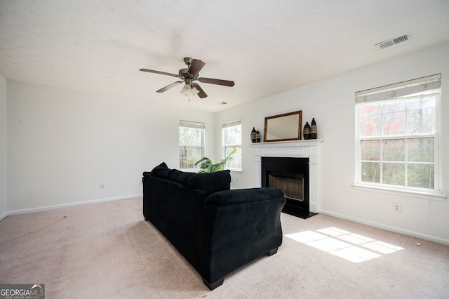 living room featuring visible vents, baseboards, a fireplace with flush hearth, light carpet, and a ceiling fan