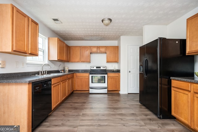 kitchen with black appliances, a sink, dark countertops, a textured ceiling, and wood finished floors