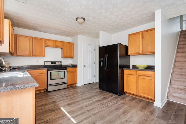 kitchen featuring a sink, electric stove, light wood-style floors, a textured ceiling, and black refrigerator with ice dispenser