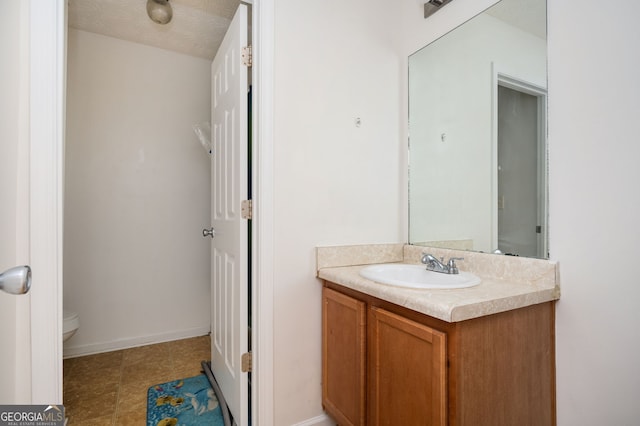 bathroom with toilet, a textured ceiling, vanity, and baseboards