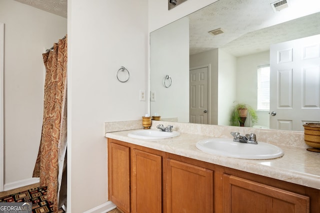 full bath with a textured ceiling, double vanity, visible vents, and a sink