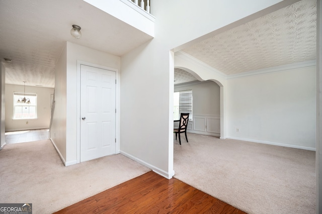 hallway featuring arched walkways, carpet flooring, crown molding, and baseboards